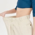 Resultados da reeducação alimentar: mulher demonstra emagrecimento saudável com calça que ficou grande após mudança de hábitos.