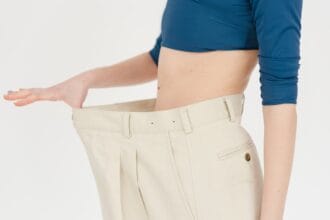 Resultados da reeducação alimentar: mulher demonstra emagrecimento saudável com calça que ficou grande após mudança de hábitos.