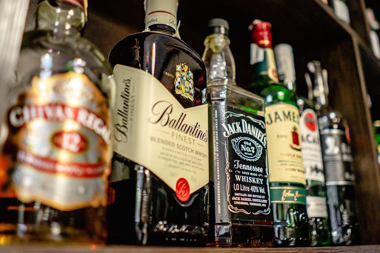 Garrafas de bebidas alcoólicas variadas em prateleira, representando substâncias tóxicas que sobrecarregam o fígado e exigem desintoxicação do organismo. A imagem mostra whiskies, destilados e outras bebidas alcoólicas que acumulam toxinas no corpo, prejudicando principalmente o fígado e os rins. O consumo excessivo de álcool é uma das principais razões para buscar chás detox e métodos naturais de desintoxicação. Estas substâncias geram radicais livres, inflamação e acúmulo de toxinas que podem ser eliminadas através de chás desintoxicantes específicos como chá verde, dente-de-leão e cardo-mariano, que protegem e limpam o fígado após exposição ao álcool.